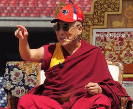 His Holiness the 14th Dalai Lama in a New England Patriots hat talking to the crowd.